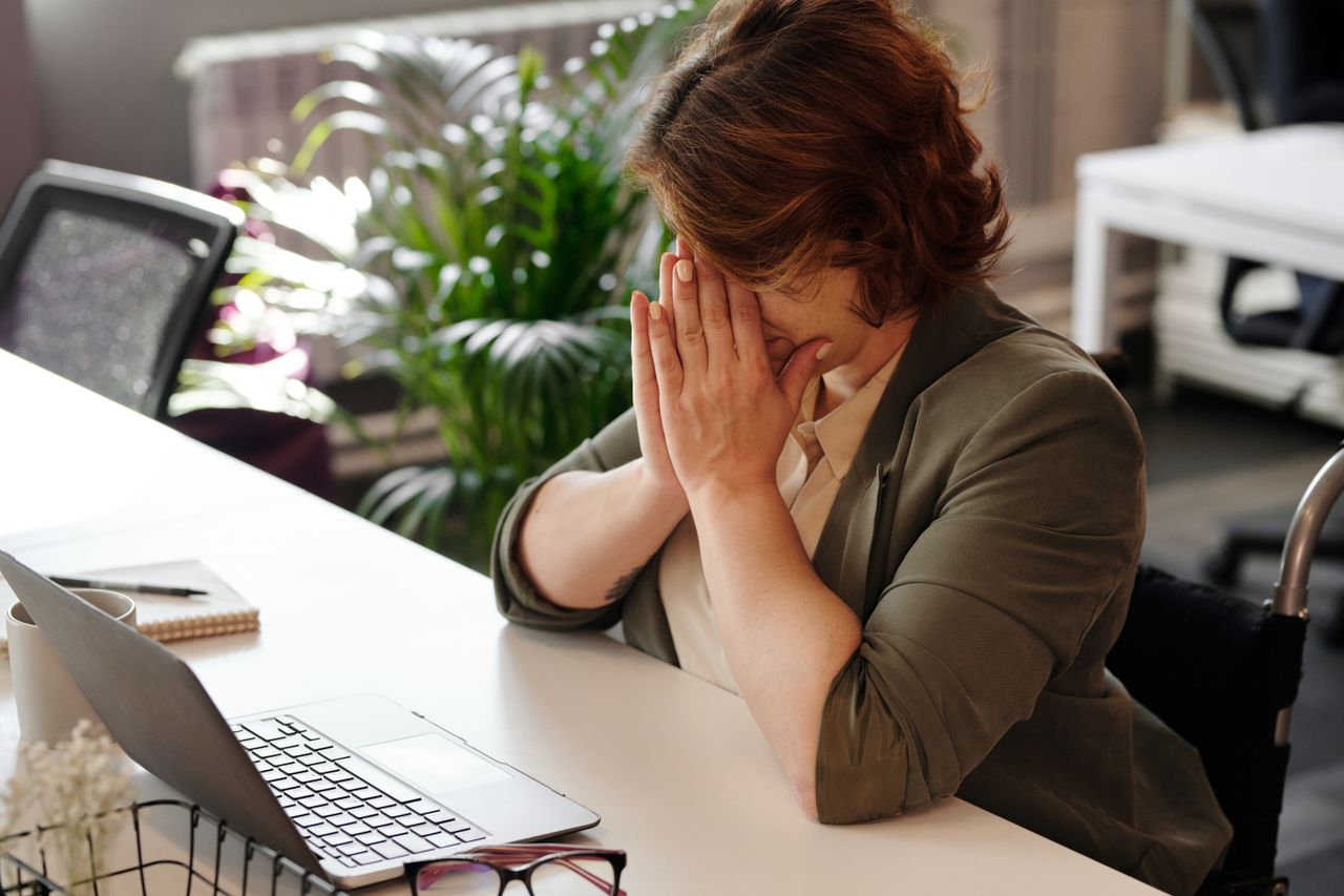 Businesswoman in wheelchair, tired at laptop, symbolizes office stress.